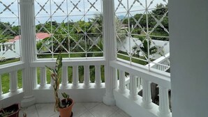 A room with a view through a white, diamond-patterned window. There are white columns and a balcony railing. - The Retreat (Lyssons)
