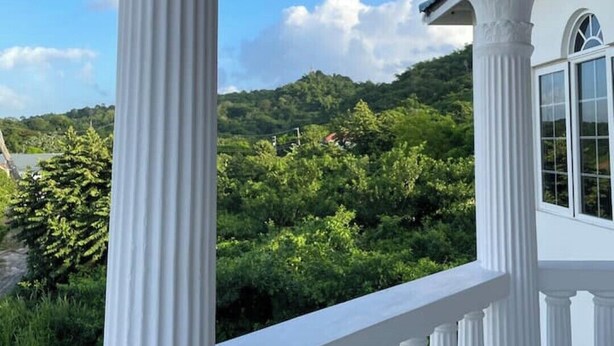A white porch with columns and a railing, overlooking a lush green landscape and hills. - The Retreat (Lyssons)