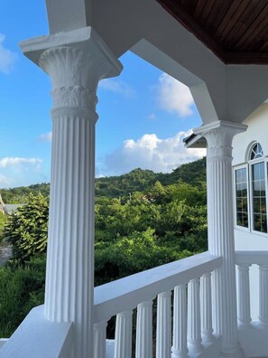 A white porch with columns and a railing, overlooking a lush green landscape and hills. - The Retreat (Lyssons)