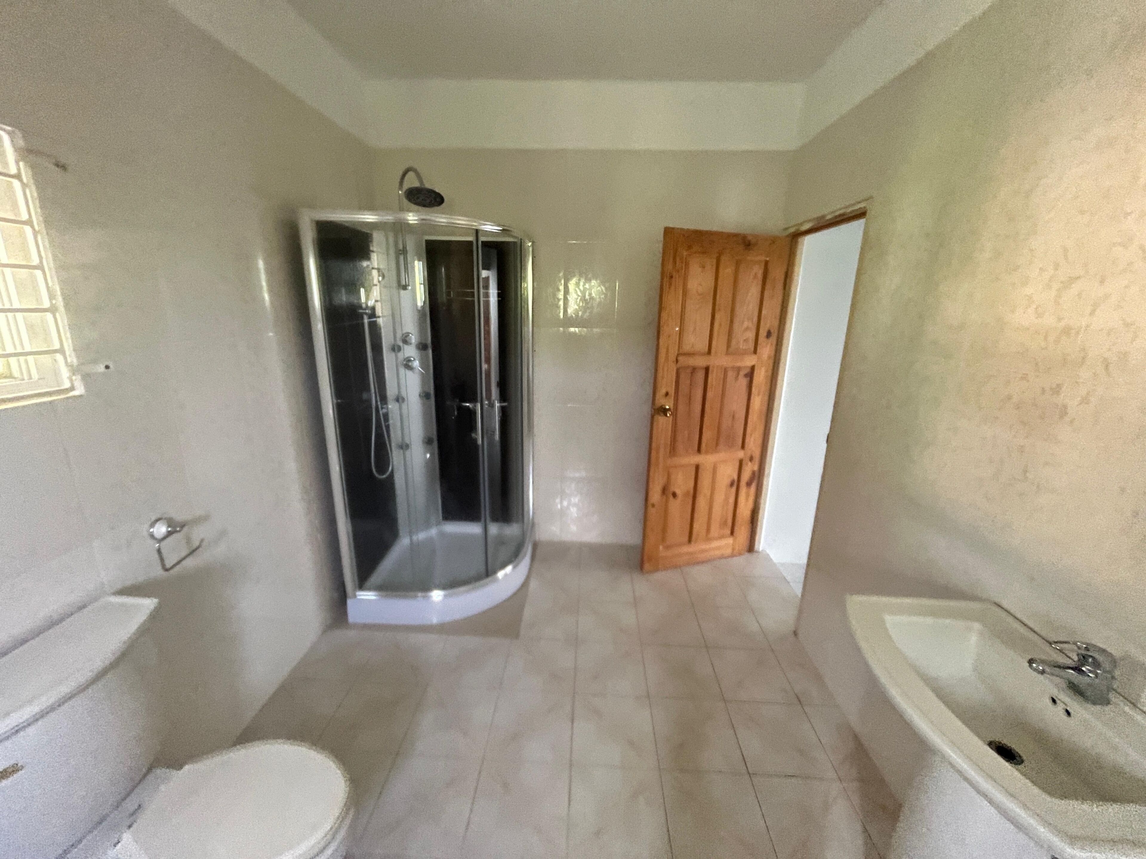 A bathroom with a glass-enclosed shower, a wooden door, a white sink, and a toilet.