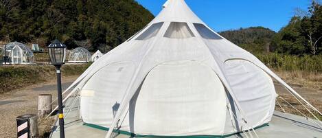 A large, white, dome-shaped tent with a conical top, set on a concrete platform with a lamp post nearby.