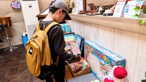 Eine Person am Tresen, mit einem gelben Rucksack, wählt Artikel aus einer bunten Boxausstellung aus.