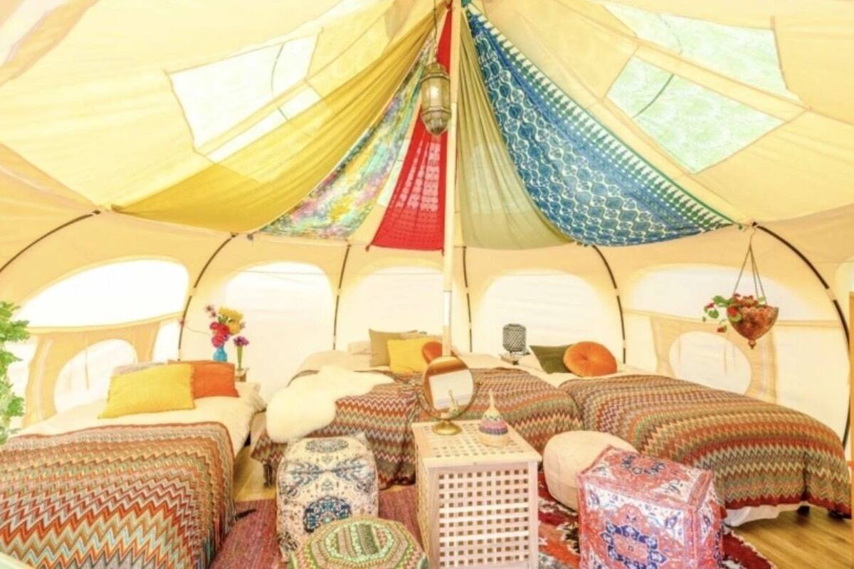 Ein zeltenähnliches Zimmer mit mehreren Betten, einer hängenden Deckenleuchte und einem kleinen Tisch.