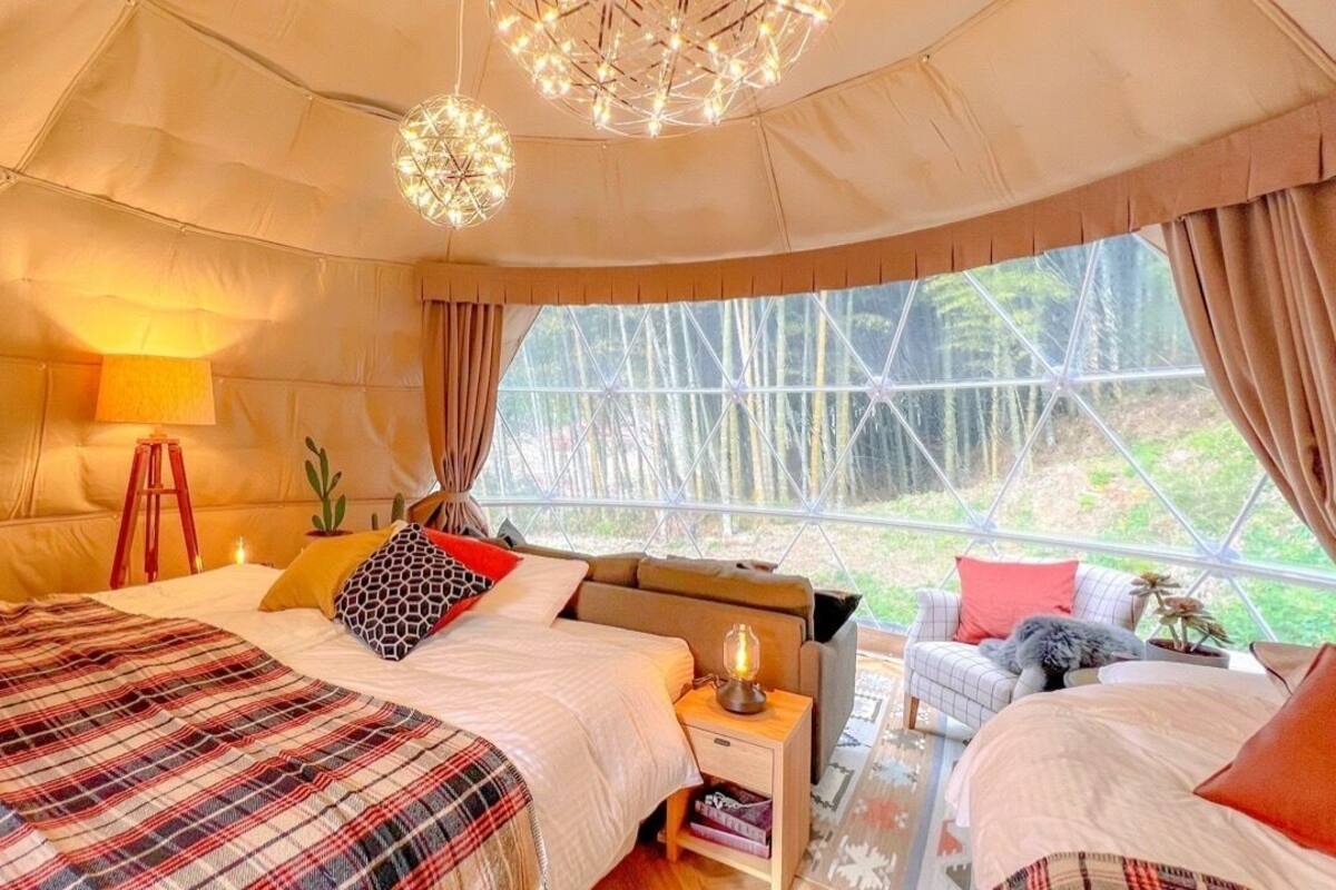Ein gemütliches Zimmer mit einem großen Bett, einem kleineren Bett, einem Nachttisch und einem Fenster mit Blick auf Grünflächen.