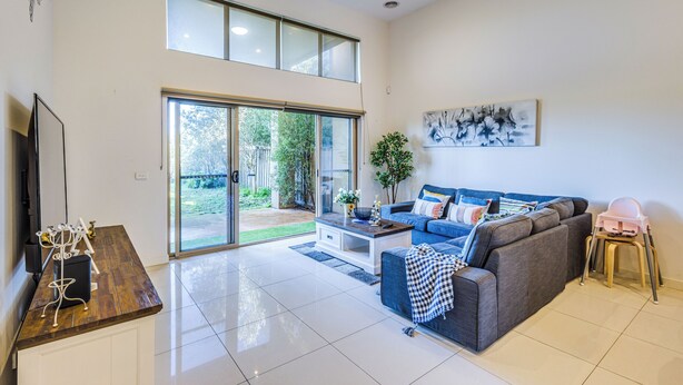 A spacious living room with a grey sofa, a coffee table, and a TV stand. - StayAU 3BR Deluxe Family Loft Point Cook (Point Cook)