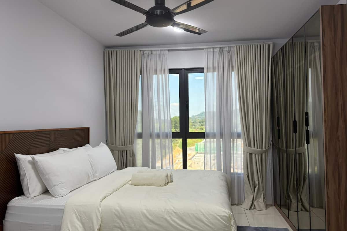 Quarto com cama, ventilador de teto, janela grande com cortinas e vista para o exterior.
