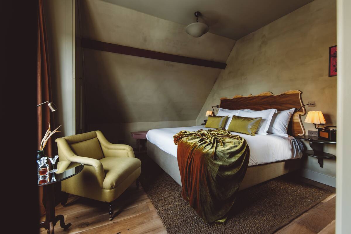 A bedroom with a bed, a chair, a table, and a lamp.