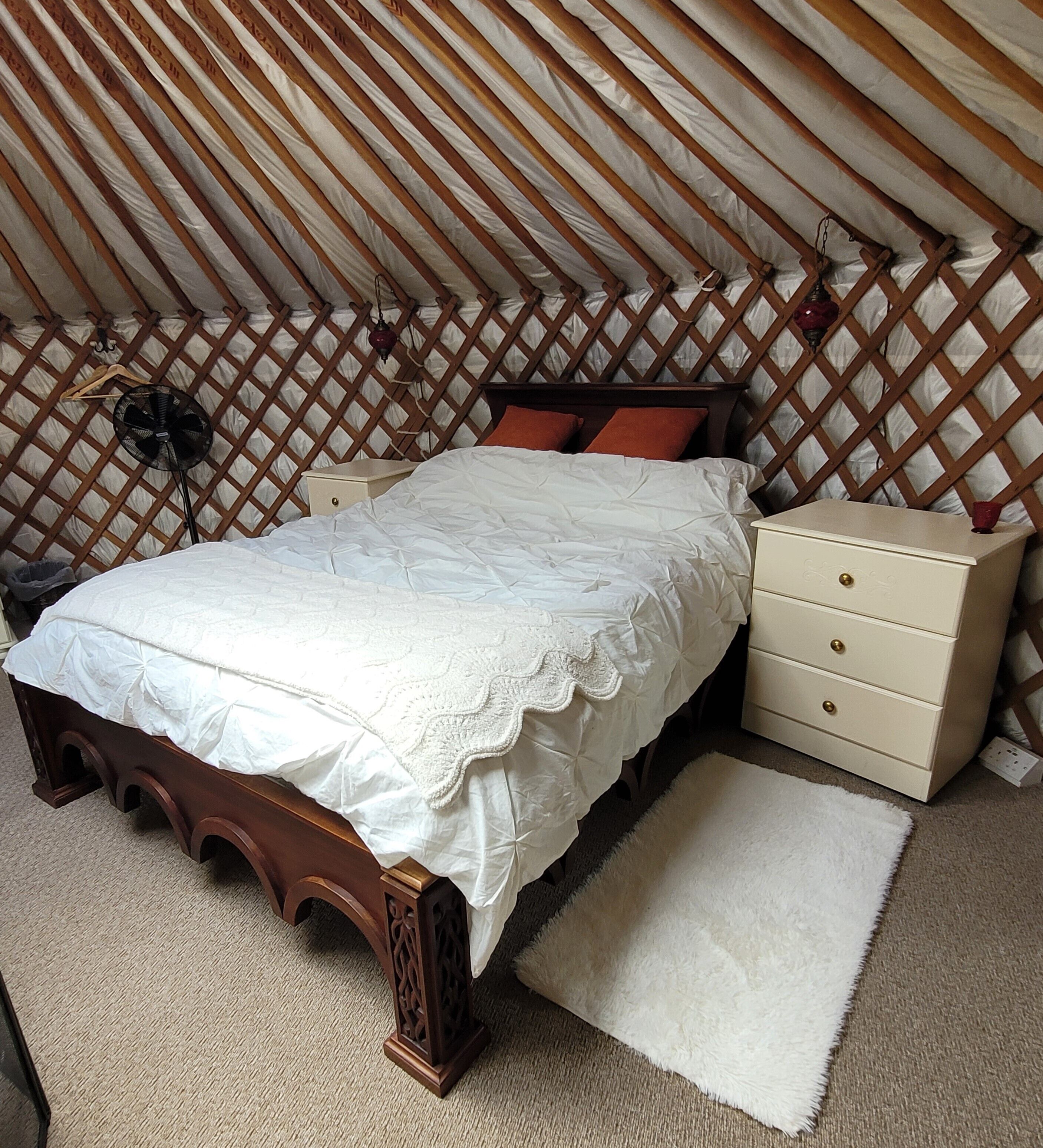 A bedroom with a wooden bed, a dresser, a nightstand, and a fan.