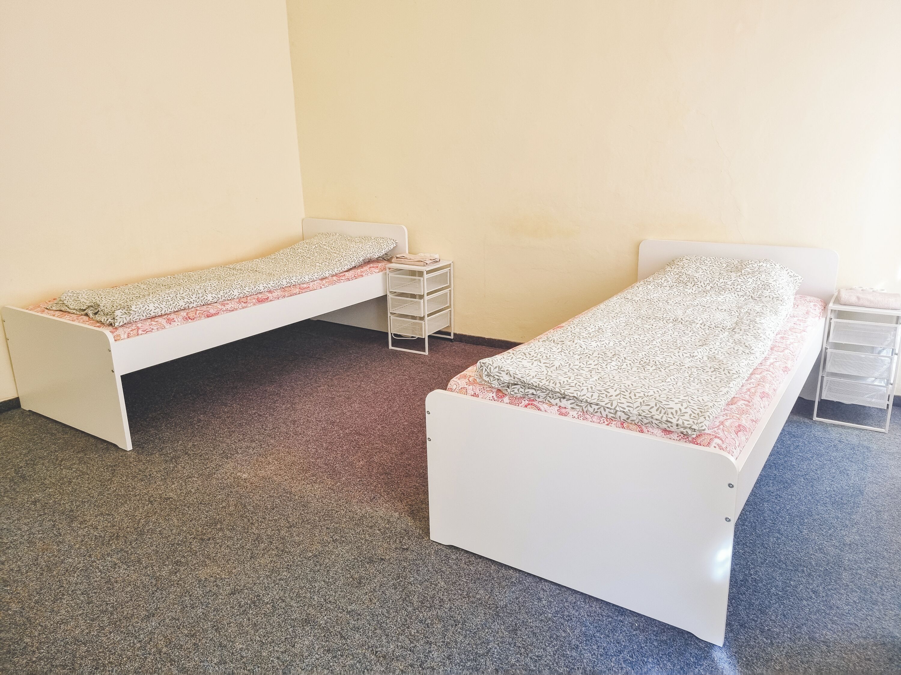 Two single beds with storage drawers, a carpeted floor, and plain walls.