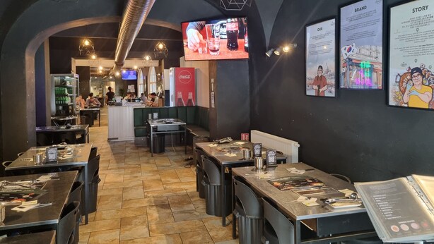 Een restaurant interieur met tafels, stoelen, een toonbank en een televisiescherm.
