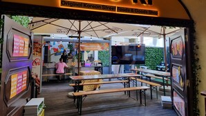 Een buitenruimte met tafels en banken, een bord waarop staat 