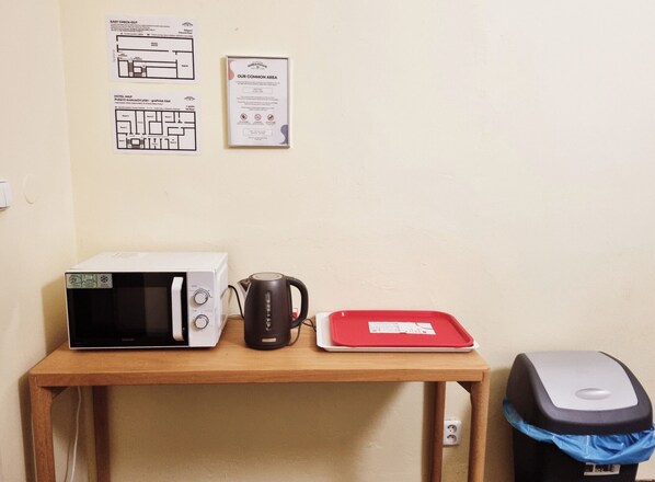 A kitchenette with a microwave, kettle, and red tray on a wooden table. - korea town (Prague)