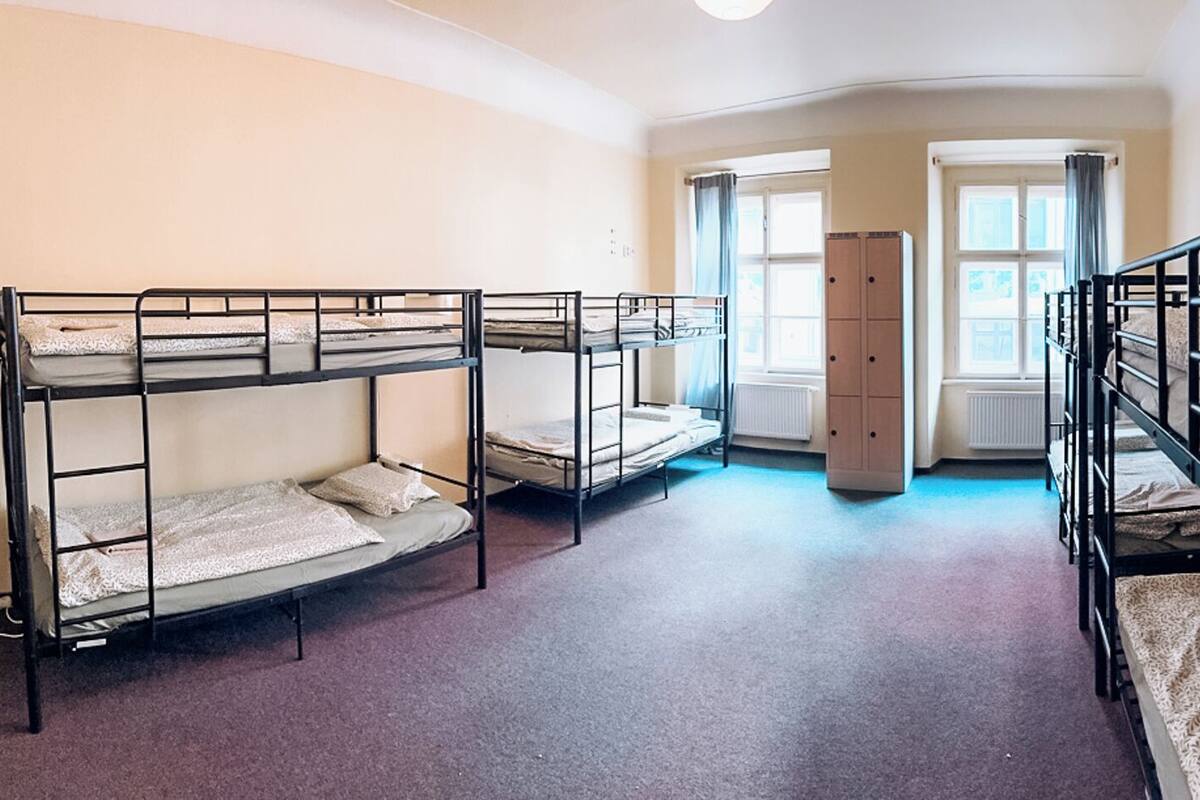 A dormitory room with bunk beds, a radiator, and a window with curtains.