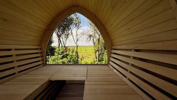 Una habitación con techo abovedado de madera, un banco y una ventana con vista a un campo verde.