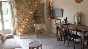 Una sala de estar acogedora con una escalera de madera, un sofá, una mesa de comedor con sillas, un televisor y un farol.