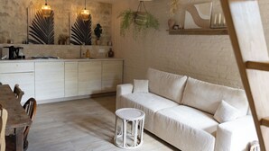 Un salón moderno con un sofá blanco, una mesita redonda y una zona de cocina con encimera blanca y plantas colgantes.