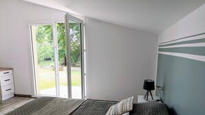 Un dormitorio con cama, mesita de noche, lámpara y vistas al exterior a través de una puerta corredera.