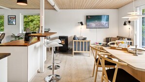 A modern kitchen with a central island, bar stools, a fireplace, and a dining area with chairs and a table. - "Mark" - 1.2km from the sea by Interhome (Græsted)
