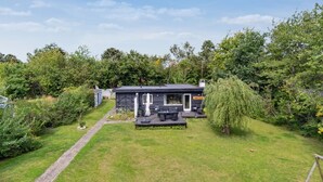 A modern outdoor seating area with a dining table and chairs, surrounded by a well-maintained lawn and dense greenery. - "Mark" - 1.2km from the sea by Interhome (Græsted)