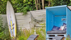A beach house with a surfboard leaning against a wooden fence, a blue cabin with a bed and pillows, and two sun loungers. - "Mark" - 1.2km from the sea by Interhome (Græsted)