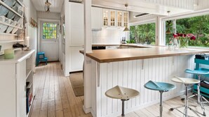 A modern kitchen with white cabinetry, a wooden countertop, and a large window offering a view of greenery.