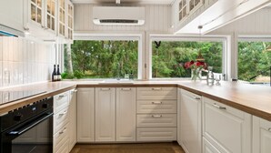 A modern kitchen with white cabinetry, a built-in oven, and a large window offering a view of greenery.