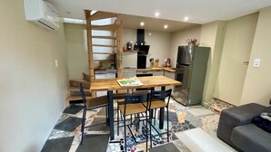 Eine kleine Küche mit Holztisch und -stühlen, einem Kühlschrank und einer Treppe, die in eine obere Ebene führt.