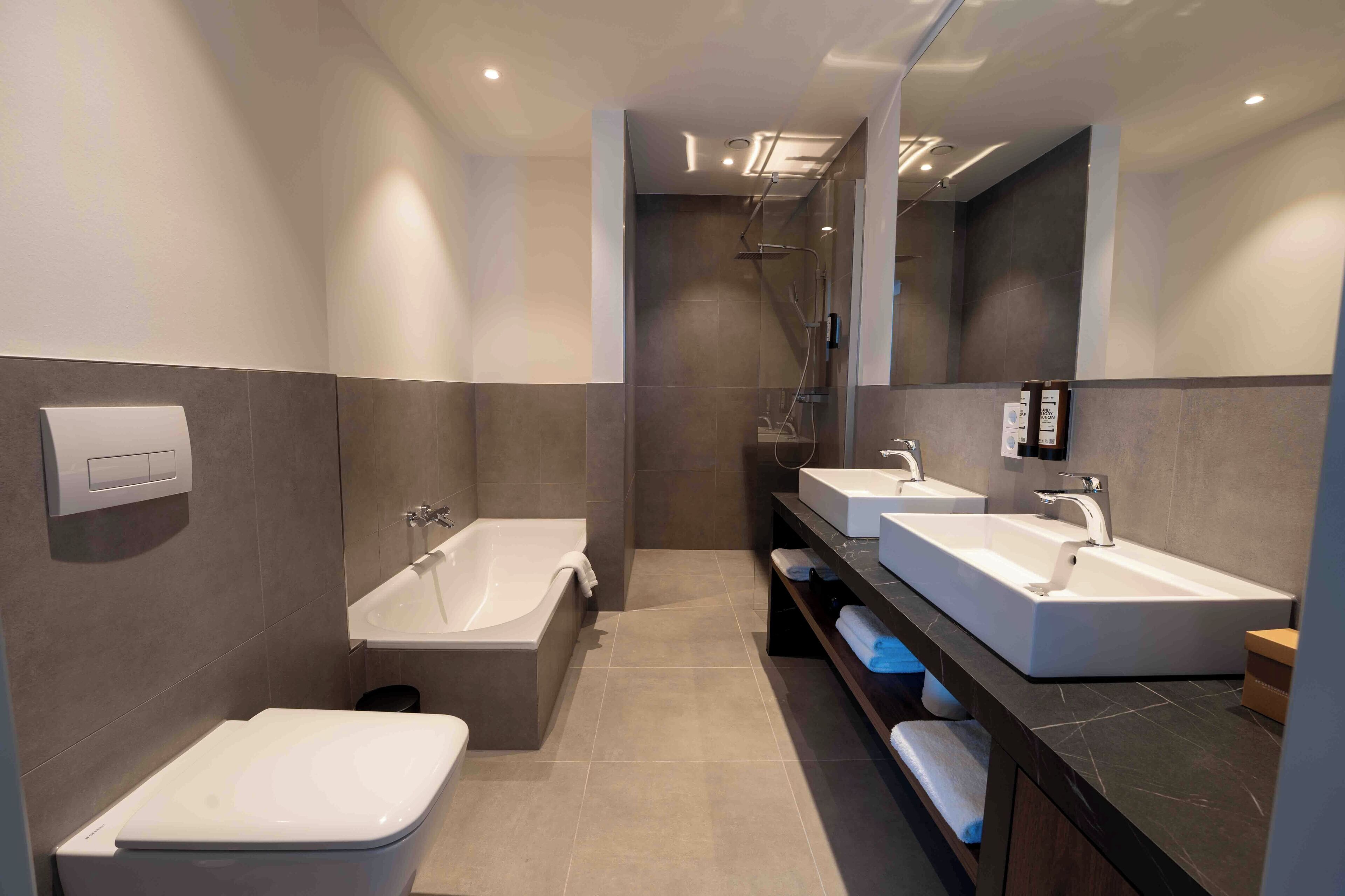 A modern bathroom with a bathtub, two sinks, and a toilet.