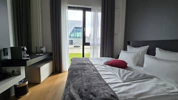 A hotel room with a bed, a desk with a computer, a trash bin, and a view of a building and a car through the window.