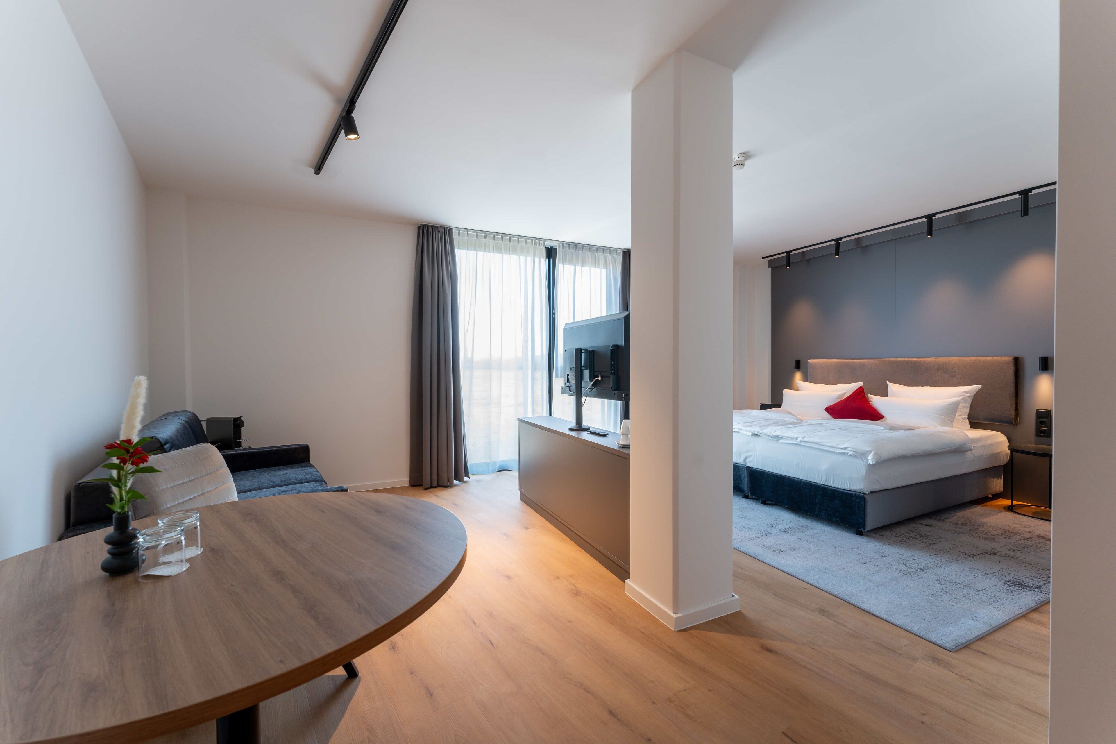 A modern hotel room with a bed, bedside table, and a dining area with a round table.