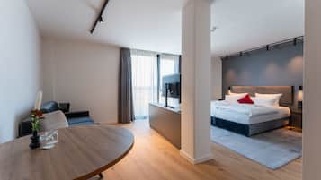 A modern hotel room with a bed, bedside table, and a dining area with a round table.