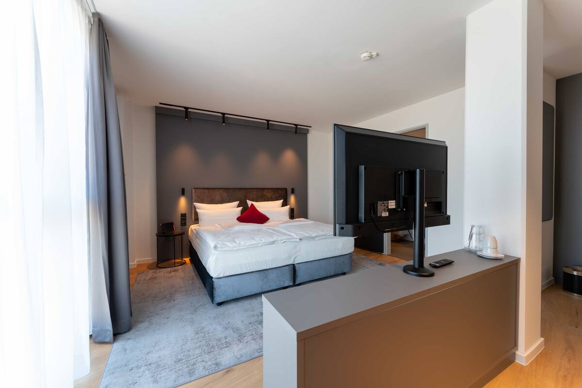 Een moderne hotelkamer met een bed, nachtkastje, televisie en een bureau.