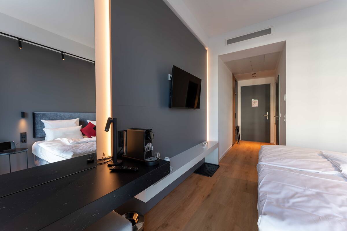 Een moderne hotelkamer met een groot bed, een bureau met koffiezetapparaat, een flatscreen televisie aan de wand en een houten vloer.