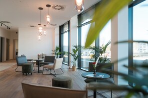 A modern interior with wooden flooring, a mix of contemporary and classic furniture, large windows offering a view of the city, and hanging pendant lights.