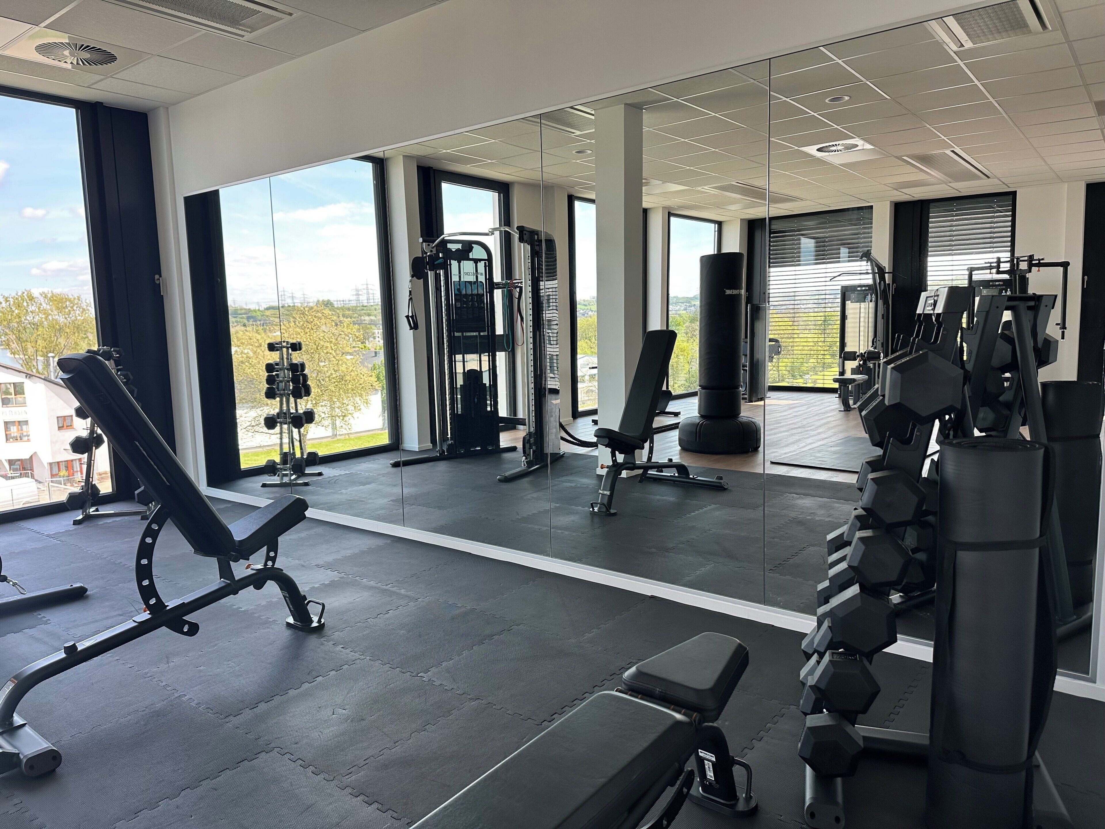 A gym with various exercise equipment, large windows, and a view of the outdoors.
