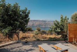 A terrace with two sun loungers, a view of a lake, and a mountainous landscape.