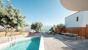 A pool area with a clear view of the sea, a wooden deck, and a table with chairs. - Istros Villa III, Infinite Blue, Pool & Whirlpool (G37Q+HX Pithari, Greece)