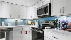 A modern kitchen with white cabinets, a microwave, a coffee maker, and a dishwasher. - Cozy corner condo, just renovated,  pool views (Fort Lauderdale)