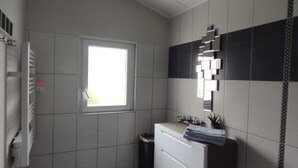 Une petite salle de bain moderne avec une fenêtre, un meuble-lavabo blanc, un miroir et une poubelle noire.