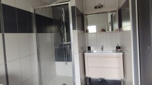 Une salle de bain moderne avec une douche à parois de verre, un meuble-lavabo blanc avec un miroir et des carreaux gris foncé au sol.