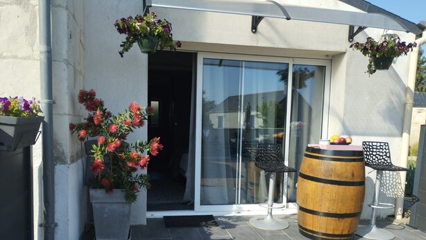 Un espace patio doté d’une porte-fenêtre coulissante, de plantes en pot, d’un tonneau en bois et de chaises en métal.