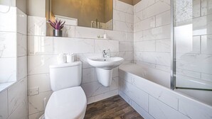 A modern bathroom with white marble tiles, a toilet, a sink, and a bathtub. - Corner Lodge - Central, refurbished & free parking (York)