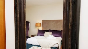 Een hotelkamer met een bed, nachtkastje, lamp en een grote spiegel.