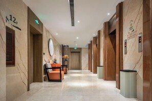 A hotel hallway with marble walls, wooden doors, and a trash bin. - Ming Yi Hotel (Zhuzhou)