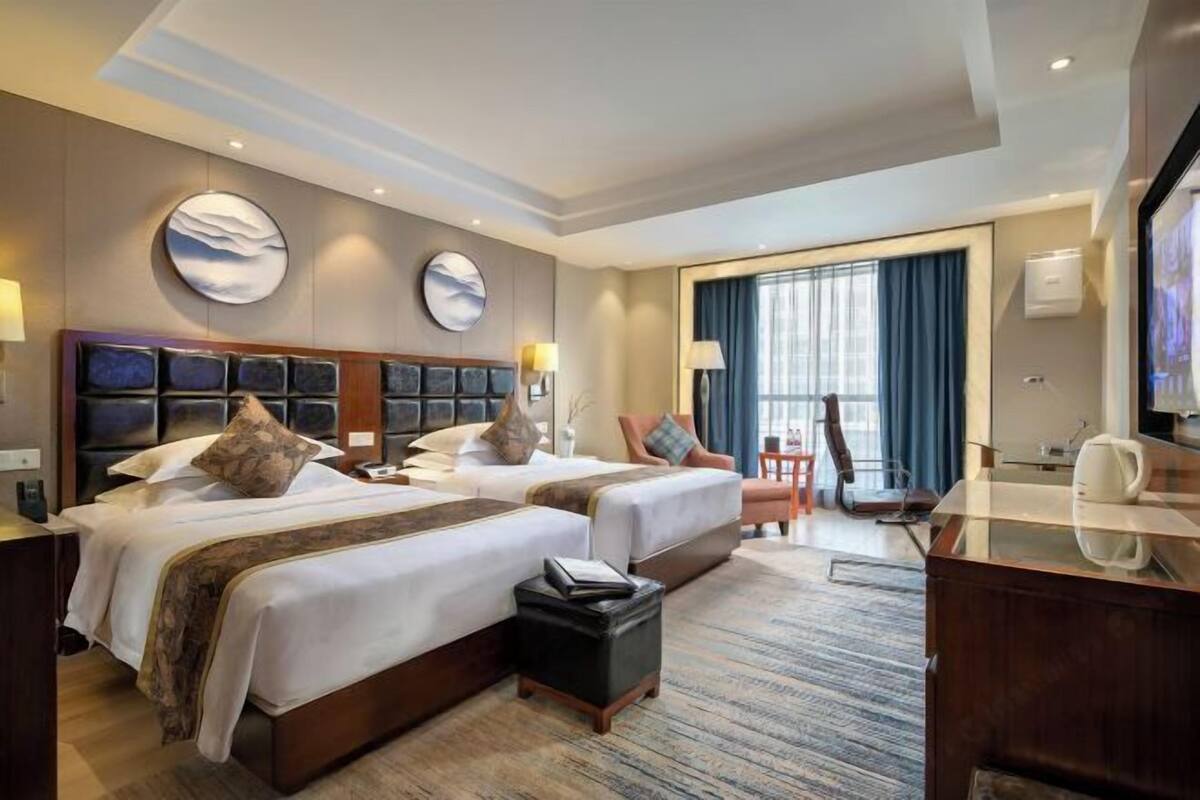 A hotel room with two beds, a desk, and a TV.