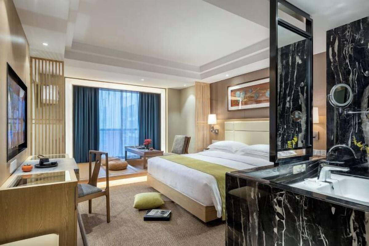 A hotel room with a bed, a desk with a chair, a large mirror, and a TV.