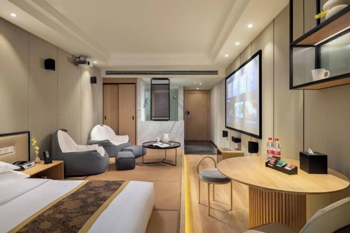 A modern hotel room with a bed, a desk, a chair, a sofa, and a TV.