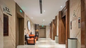 A hotel lobby with marble flooring, wooden paneling, a reception desk, and a seating area with orange chairs. - Ming Yi Hotel (Zhuzhou)