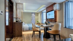A modern hotel room with a dining area, a large TV screen, and a wooden floor. - Ming Yi Hotel (Zhuzhou)