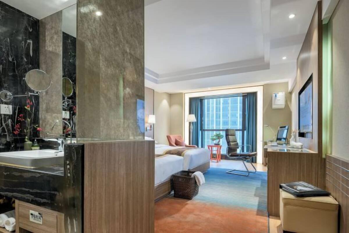A hotel room with a marble bathroom, a bed with pillows, a desk with a computer, and a window with a view.